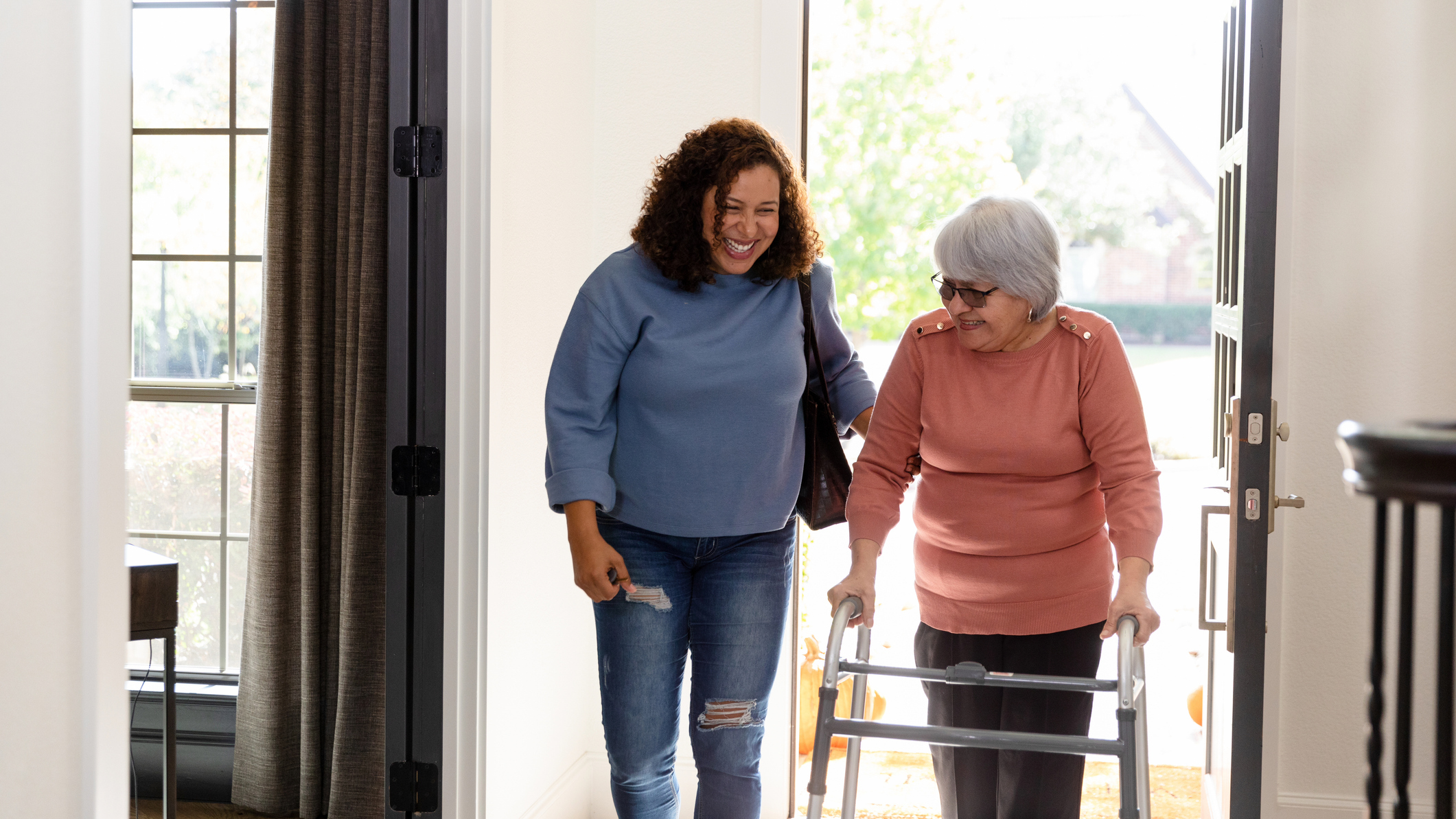 Two smiling women, one using a walker, enter a home