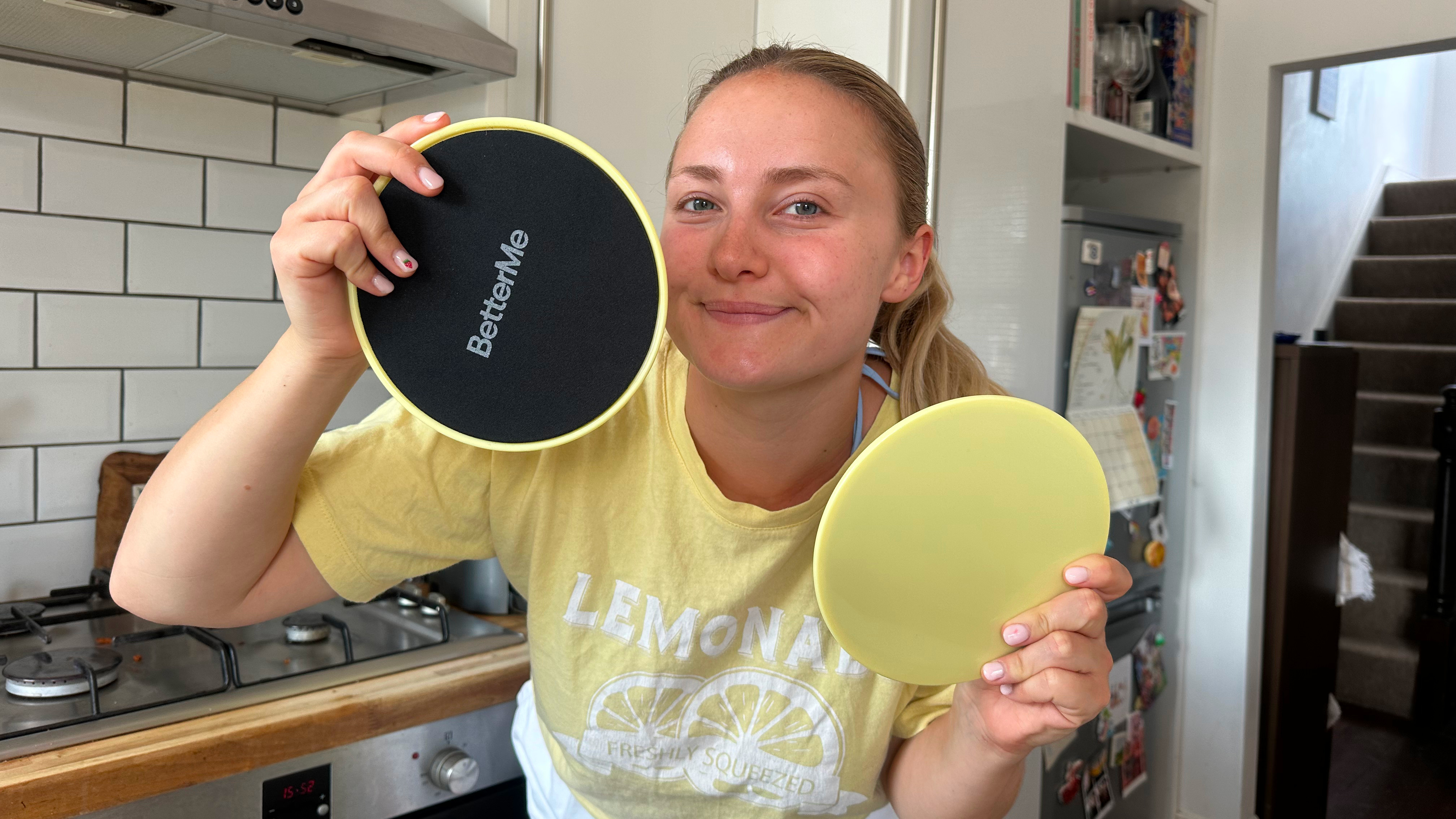 Woman holds two black and yellow discs up to camera. She is in a kitchen