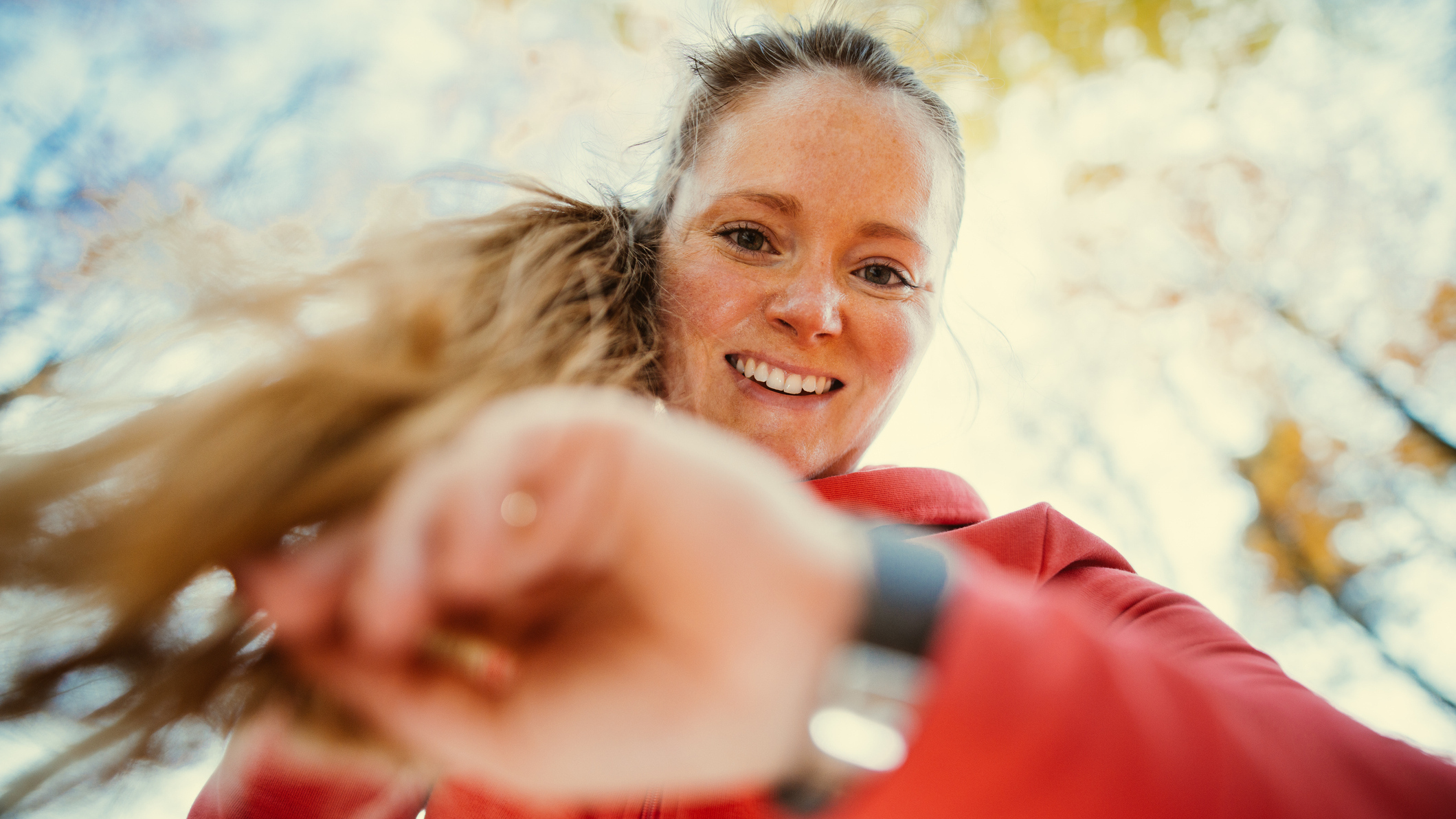 Woman looks at her watch. She is outside with trees overhead