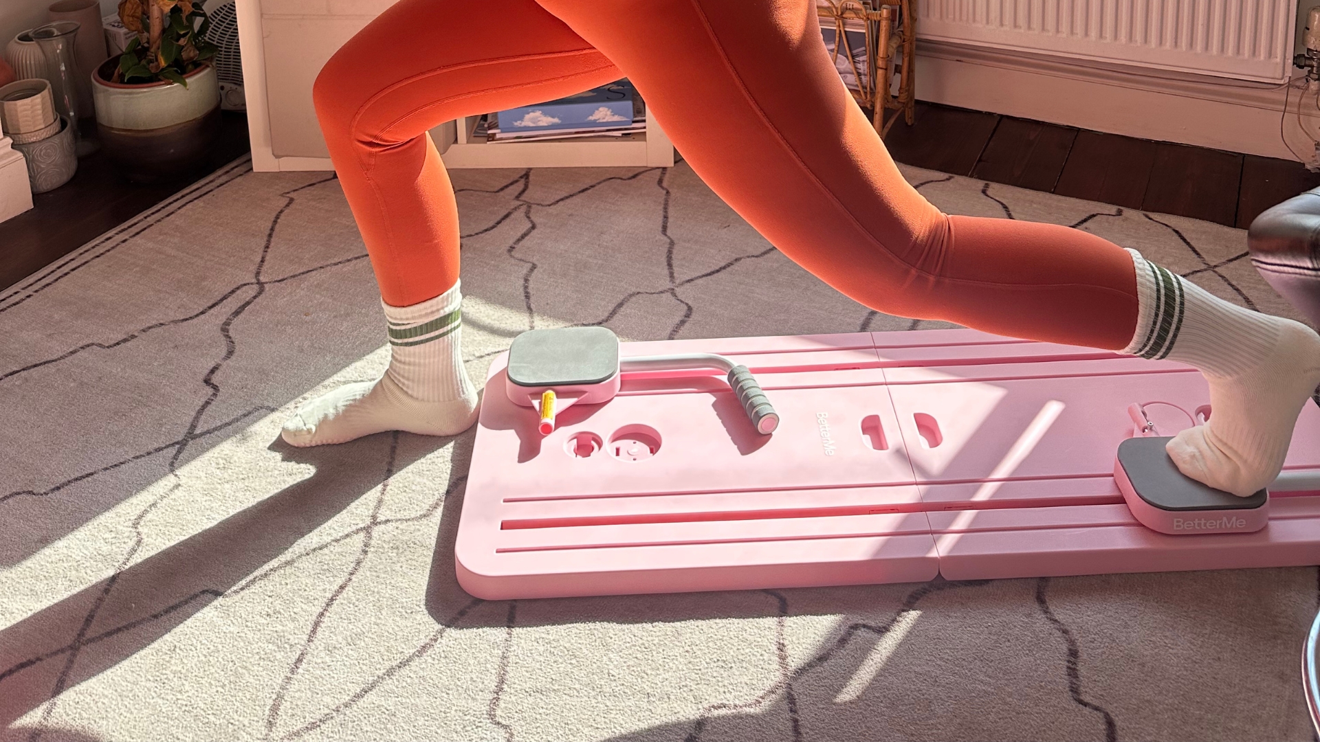 Bottom half of person exercising using a Pilates board, with one foot on a slider on the board and the foot behind the person&rsquo;s front foot