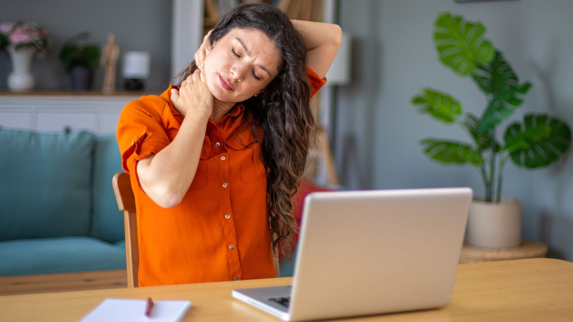 woman holds onto painful neck in front of laptop