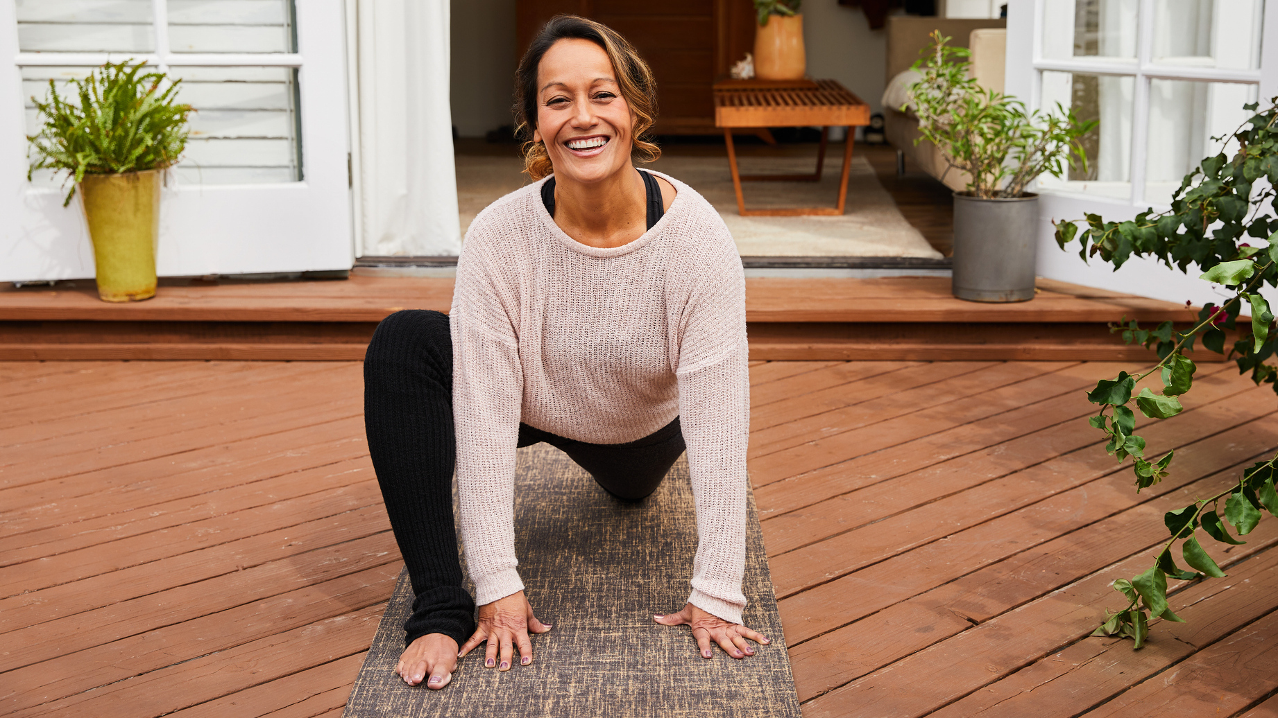 Smiling woman outside on deck stretching her hips in a low lunge